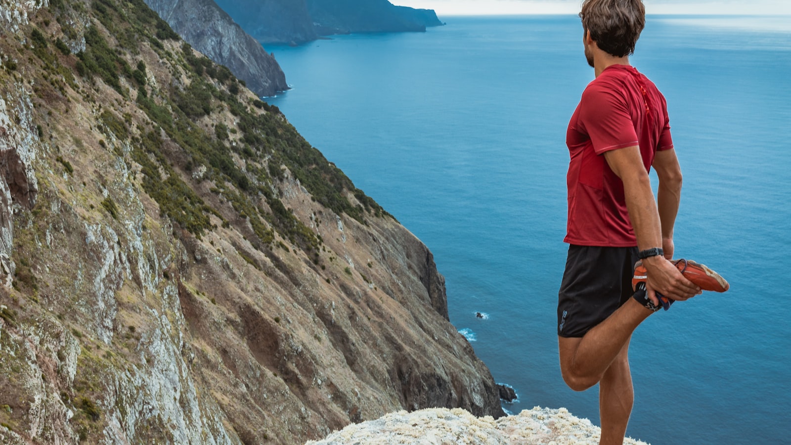 Coureur de trail sur un sentier rocheux face à un paysage de montagne et d'océan
